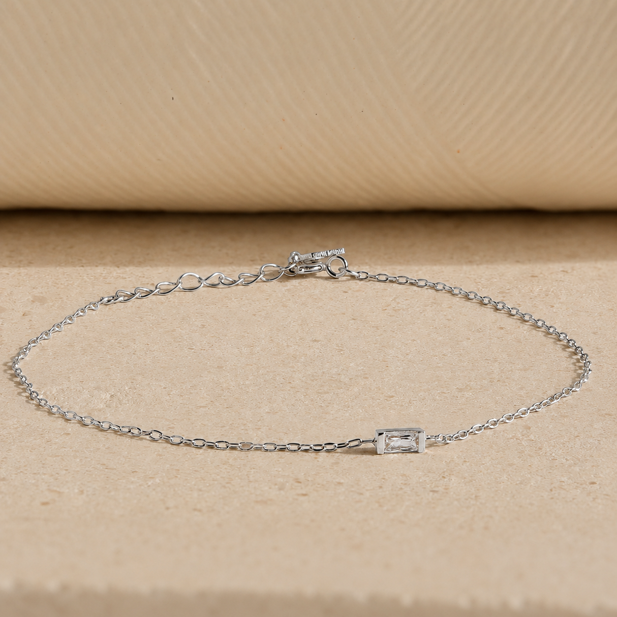 Silver bracelet with a small rectangular gemstone on a beige background